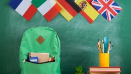 Güner Rucksack auf Tisch mit Büchern und Schreibzubehör und den Flaggen von Großbritannien, Spanien, Deutschland, Italien und Frankreich im Hintergrund.