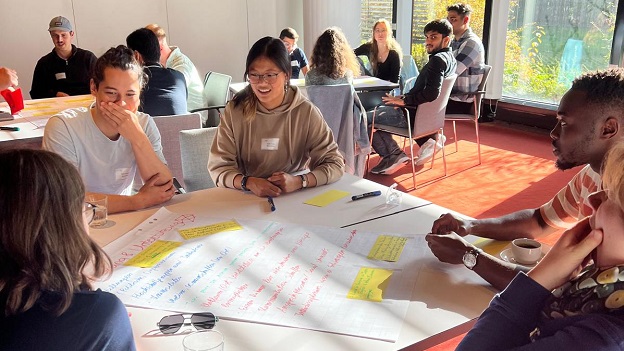 EmS-Standortaktive sitzen an Tischen und beschriften ein Flipchart Papier