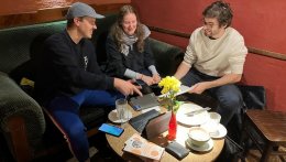 3 junge Studierende sitzen in einem Café an einem Tisch mit einem Tablet, Notizbüchern und Europa macht Schule Flyern und besprechen alles für das kommende EmS-Programmjahr in Jena